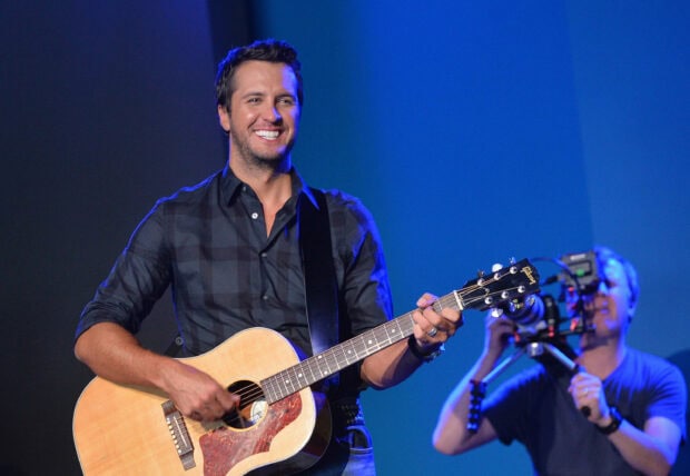 Luke Bryan playing an acoustic guitar and smiling during a live performance, 2K Desktop Wallpaper