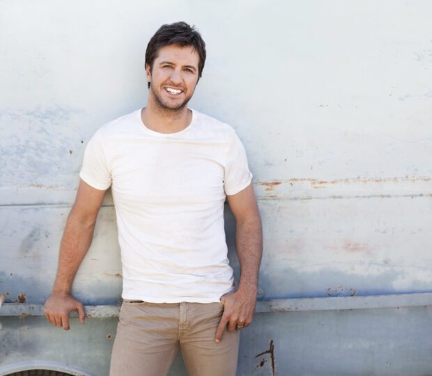 Luke Bryan smiling casually standing against a weathered wall outdoors, HD Desktop Wallpaper