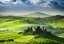 A scenic view of green hills surrounded by trees and rural houses at dawn, 2K Desktop Wallpaper