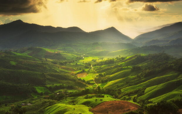 A scenic view of green hills with sunlight shining through cloudy skies, HD Desktop Wallpaper