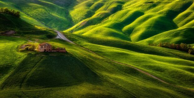 A rustic farmhouse is surrounded by lush green hills under soft sunlight, HD Desktop Wallpaper