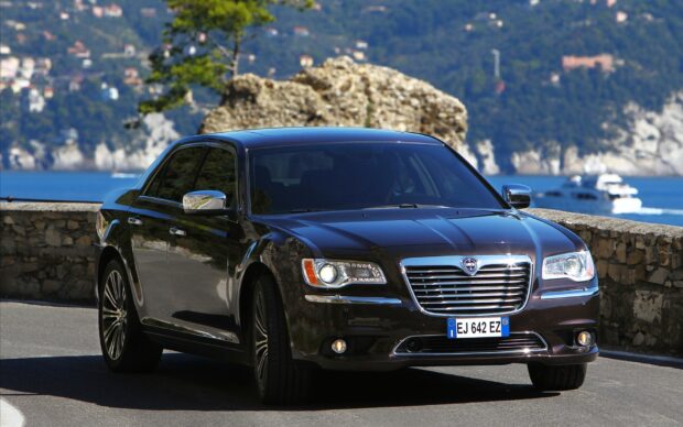 A black Lancia car driving along a scenic coastal road, HD Desktop Wallpaper