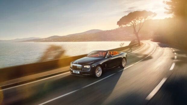 A Rolls Royce Dawn driving along a sunny coastal road during sunset with two passengers inside, 4K Desktop Wallpaper