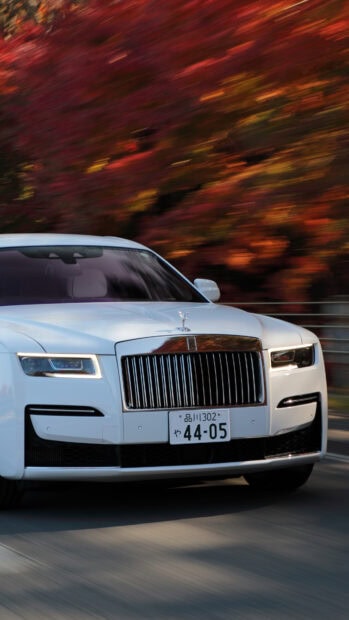 A white Rolls Royce Ghost is driving past colorful fall trees, 4K Phone Wallpaper