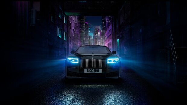 A Rolls Royce Ghost is parked in a dark alley with bright headlights and city lights in the background, 4K Desktop Wallpaper