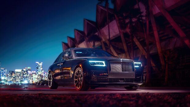 A Rolls Royce Ghost shines under urban nightlights next to modern architecture, 4K Desktop Wallpaper