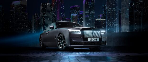 A sleek Rolls Royce Ghost shines against a vibrant city skyline at night featuring illuminated buildings, 2K Desktop Wallpaper