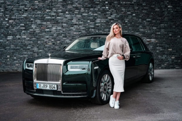A woman stands confidently next to a black Rolls Royce Phantom on a damp street, 2K Desktop Wallpaper