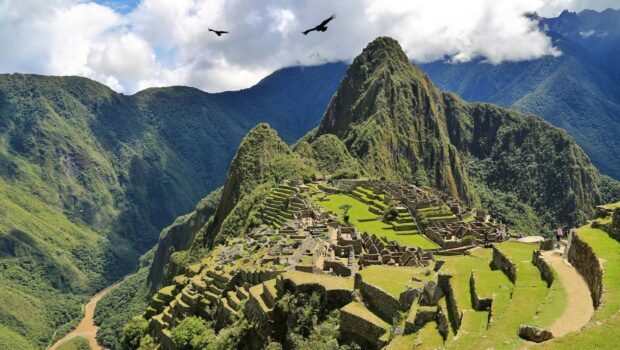 Ancient Machu Picchu ruins surrounded by mountains and flying birds in clear sky