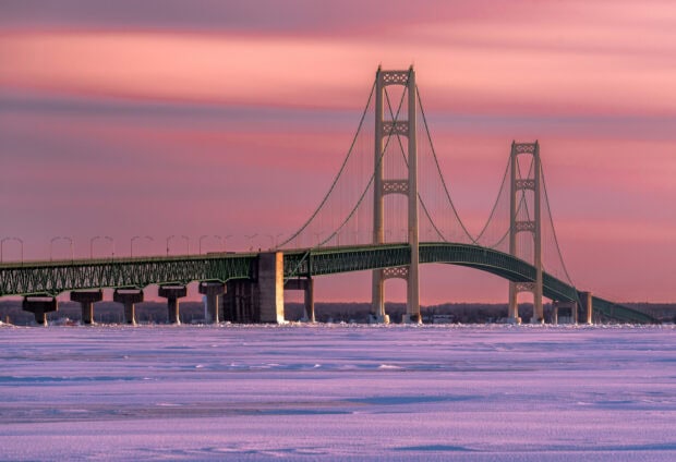 The Mackinac Island bridge stretches over frozen water under a pink sunset sky, HD Desktop Wallpaper