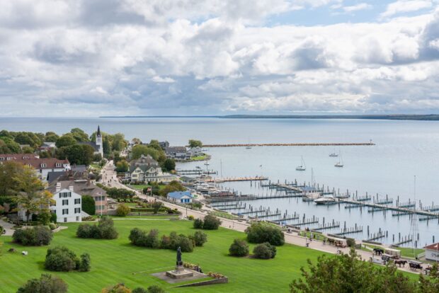 A scenic view of Mackinac Island showing the harbor, boats, and lush green areas under a cloudy sky, HD Desktop Wallpaper