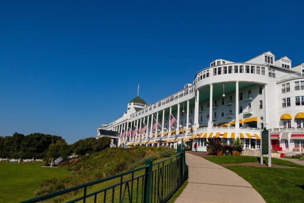 The image shows a large white hotel on Mackinac Island surrounded by clear skies and greenery, HD Desktop Wallpaper