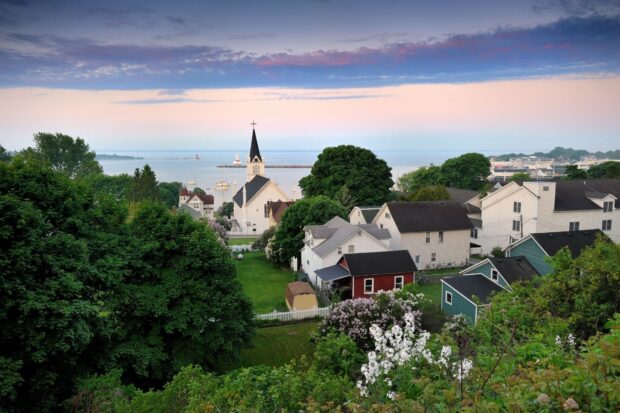 A scenic view of Mackinac Island with houses, trees, and a church near the shoreline, HD Desktop Wallpaper