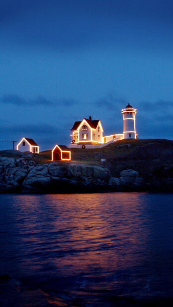 A Maine lighthouse glowing with lights stands on rocky shores under a twilight sky, HD Mobile Wallpaper
