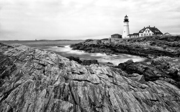 A black and white photo of rocky shore with a lighthouse and buildings in Maine Wallpapers, 2K Desktop Wallpaper