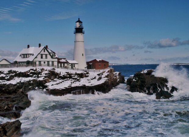The Maine lighthouse stands tall on a snowy rocky coast with waves crashing nearby, HD Desktop Wallpaper