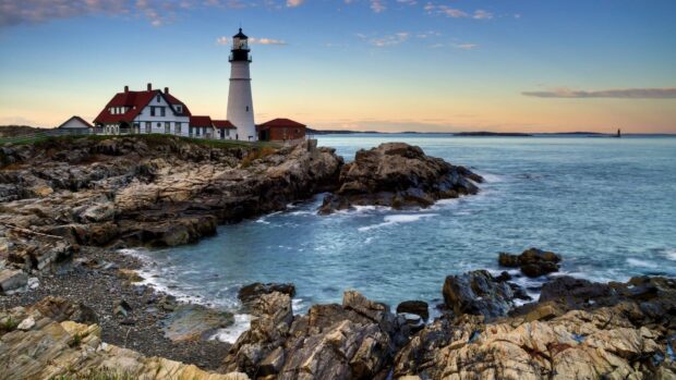 A lighthouse stands on the rocky Maine coast during a calm evening with gentle waves, HD Desktop Wallpaper