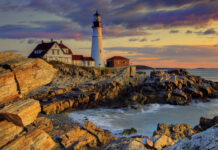 The image shows Maine with a lighthouse on the rocky coastline during sunset, 2K Desktop Wallpaper