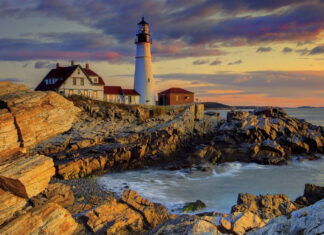 The image shows Maine with a lighthouse on the rocky coastline during sunset, 2K Desktop Wallpaper