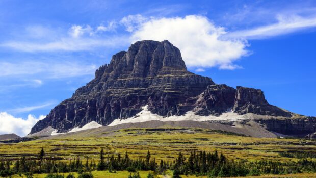 A large rocky mountain with patches of snow under a blue sky in Glacier National Park, 4K Desktop Wallpaper