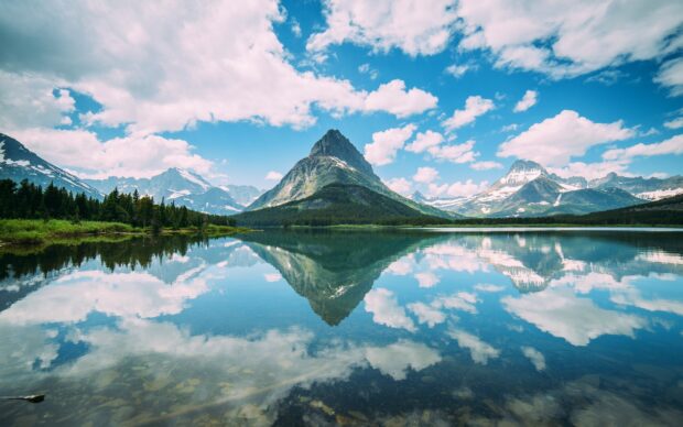The mountains of Glacier National Park are reflected perfectly in a calm lake under a bright sky, HD Desktop Wallpaper