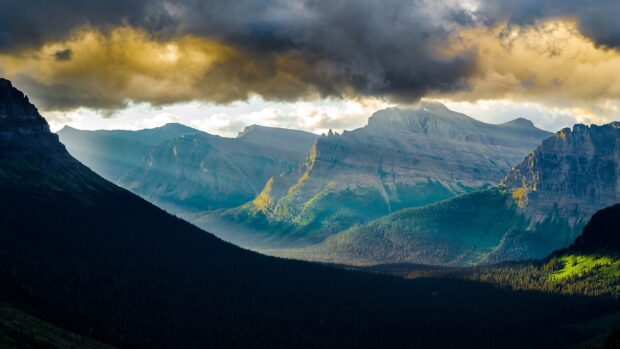 The sun casts light over the majestic peaks of Glacier National Park mountains at sunset, 4K Desktop Wallpaper