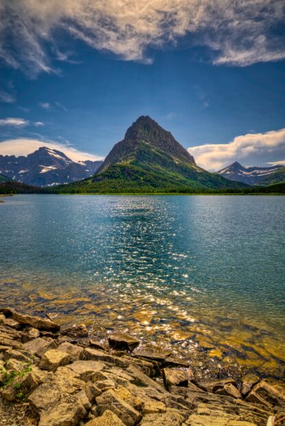 A clear lake reflects the towering mountain in Glacier National Park under a blue sky, HD Phone Wallpaper