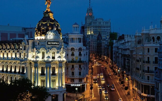 The Metropolis building stands illuminated along a busy street in Spain with a deep blue night sky, 2K Desktop Wallpaper