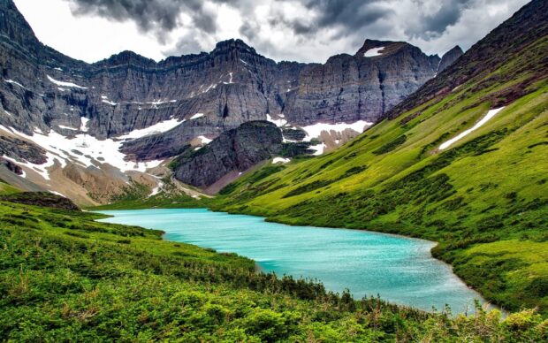 A serene Montana scene features a turquoise lake surrounded by green hills and rugged mountains, Desktop Wallpaper