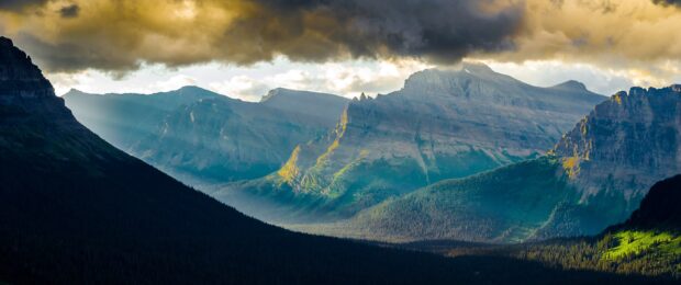 The Montana mountains show sunlight breaking through dark clouds over the forest, 2K Desktop Wallpaper