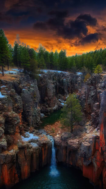 A waterfall flows through rocky cliffs surrounded by pine trees at sunset scenery wallpapers, 4K Phone Wallpaper