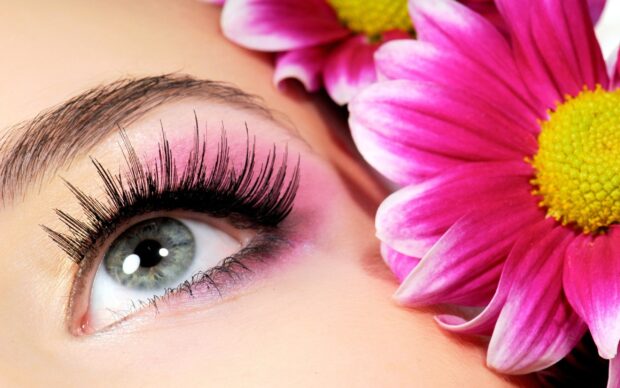 Close up of eye makeup with long eyelashes and pink eyeshadow near a pink flower