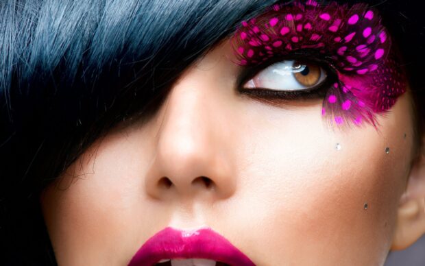Close up of makeup featuring pink feather eyelashes and vibrant lipstick on a woman