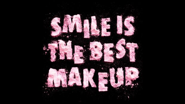 Pink makeup powder forming the phrase smile is the best makeup on black background