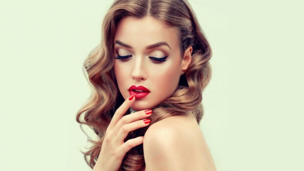 Woman wearing makeup with red lips and nails looking down contemplatively