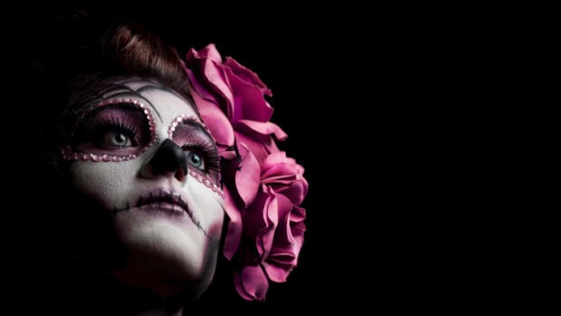 Woman wearing sugar skull makeup surrounded by pink flowers and makeup on face