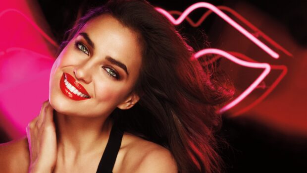 A woman with bright red lipstick showcasing makeup in front of neon lips lighting