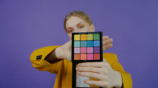 A woman holding a colorful eyeshadow palette with makeup applied on her eyes
