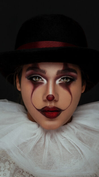 Woman with artistic clown makeup wearing a black hat and white lace collar