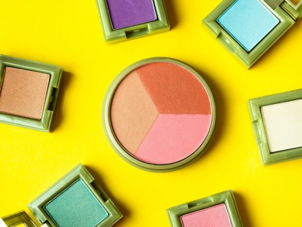 Colorful eyeshadow makeup palette displayed on bright yellow surface with blush compact