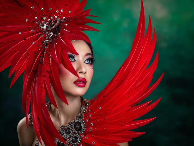 Woman with vibrant makeup and red feather accessories showcasing creative makeup
