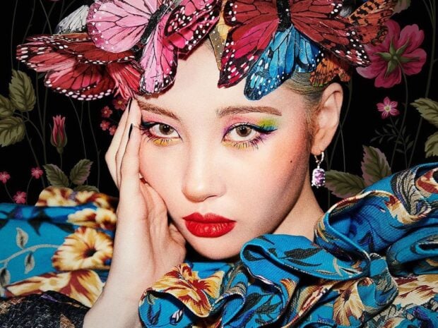 A woman with butterfly eye makeup and bold red lips wearing a floral blue outfit and butterfly headpiece