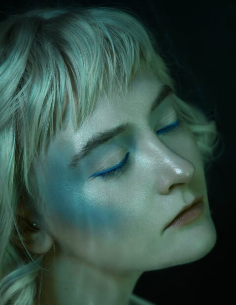 A close up of a woman with blue eyeliner and detailed makeup on her face