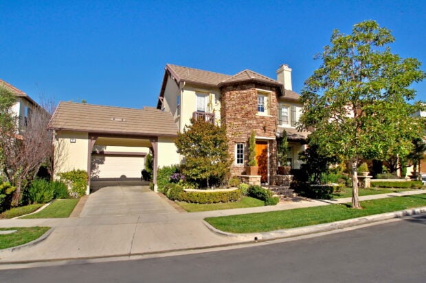Spacious Malibu California home with stone facade and lush greenery under a clear blue sky