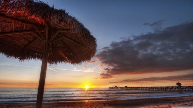 Sunset over Malibu California with a wooden beach umbrella and pier in view