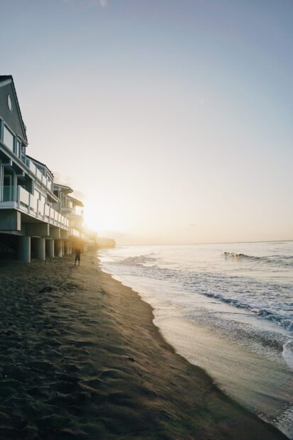 A person walking on the beach near Malibu California during sunset with houses lining the shore