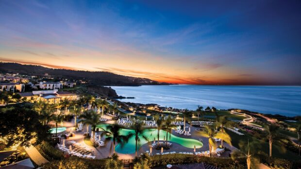 A scenic view of Malibu California featuring a coastline resort with a glowing pool and sunset sky