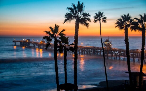 Sunset view of Malibu California pier with palm trees and calm ocean waves