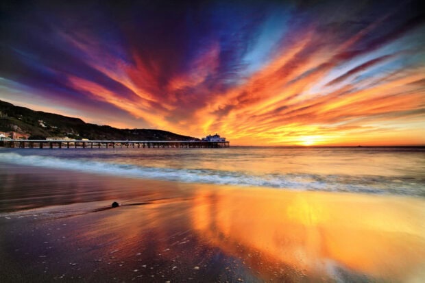 Vibrant Malibu California sunset with pier and ocean waves reflecting colorful sky
