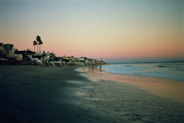 A serene Malibu California coastline at sunset with houses and palm trees lining the beach